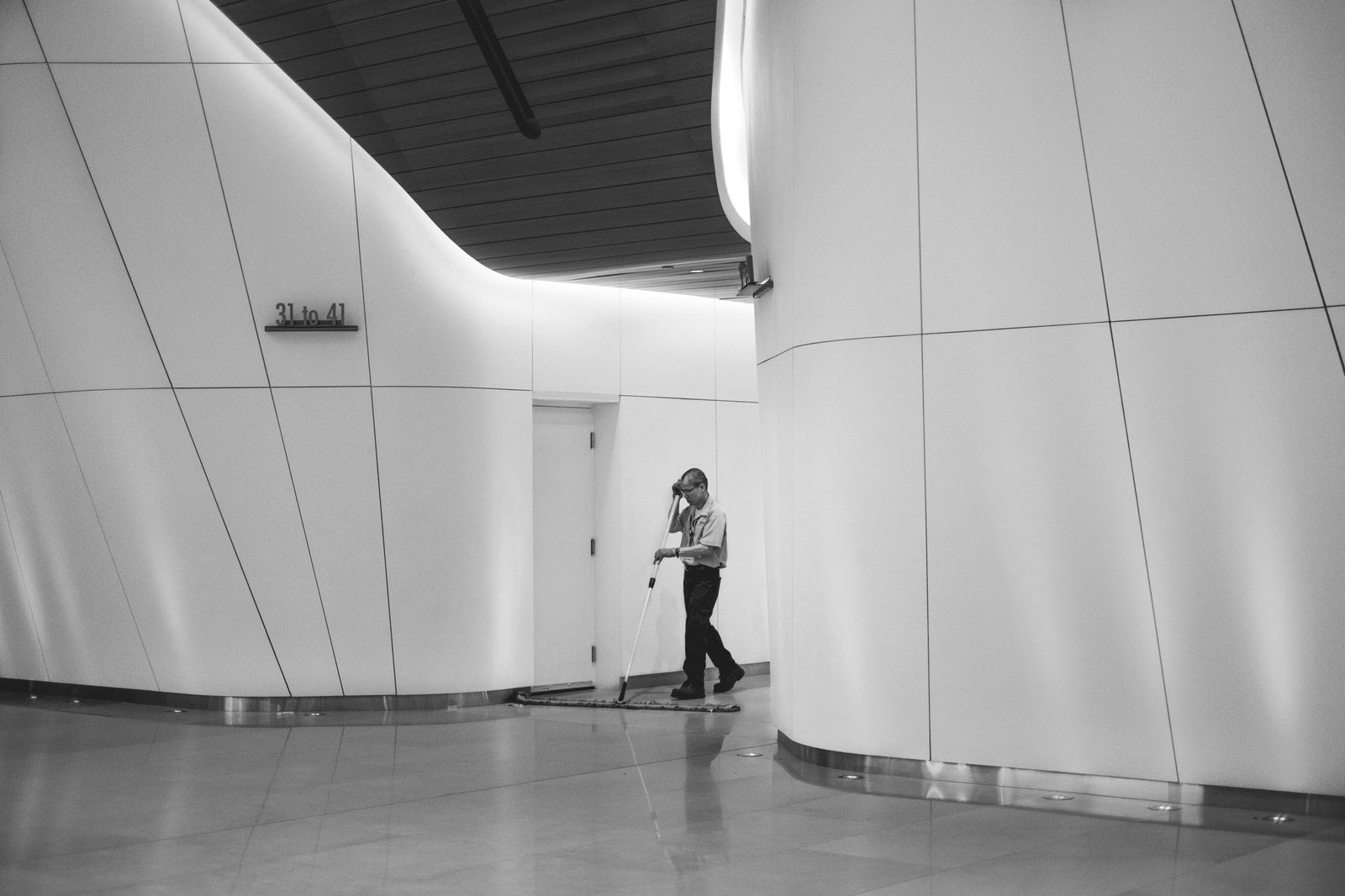 Maintenance worker mopping in a curved-white-wall architectural interior